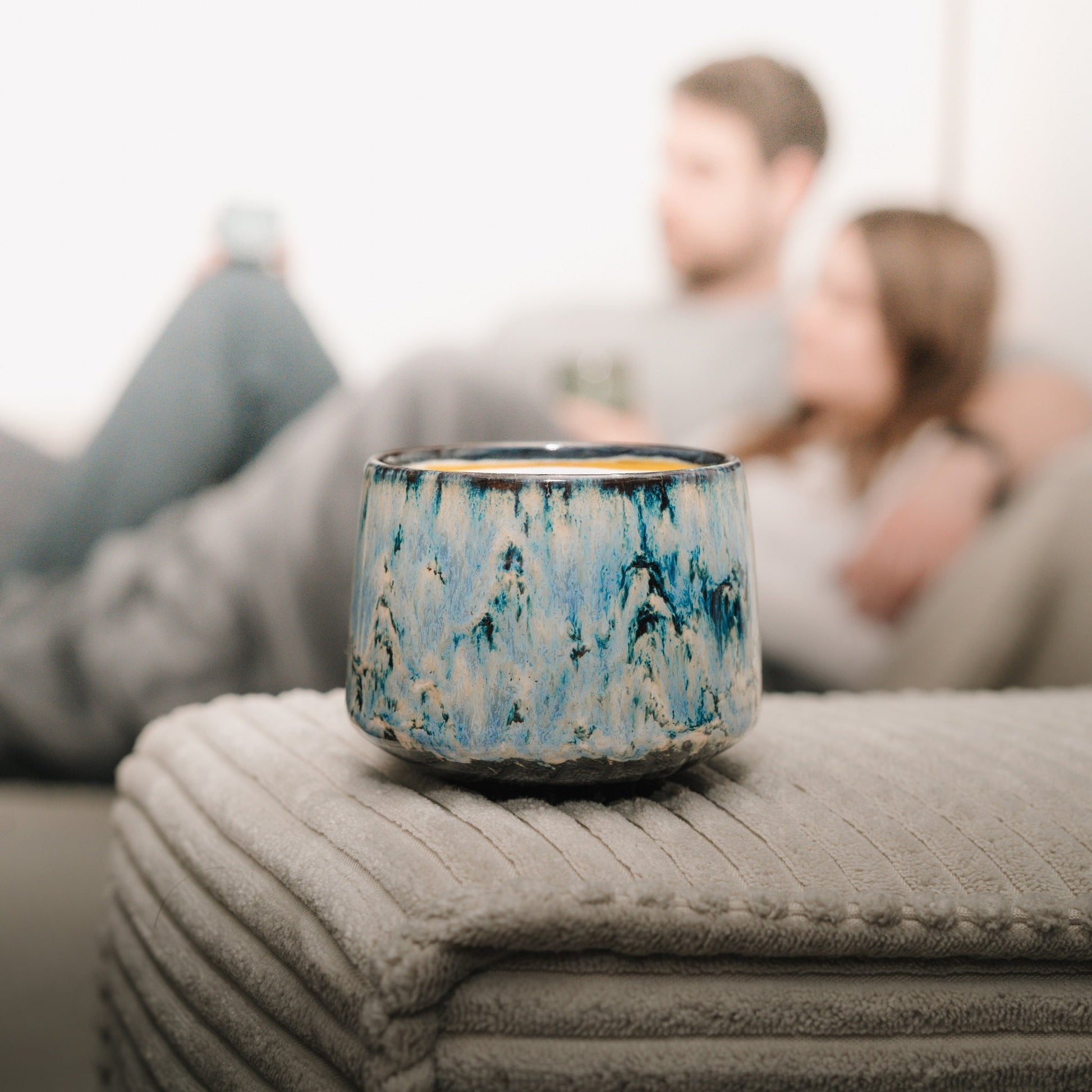 Cappuccino Tasse präsent im Vordergrund. Im Hintergrund Pärchen, dass Kaffee genießt.