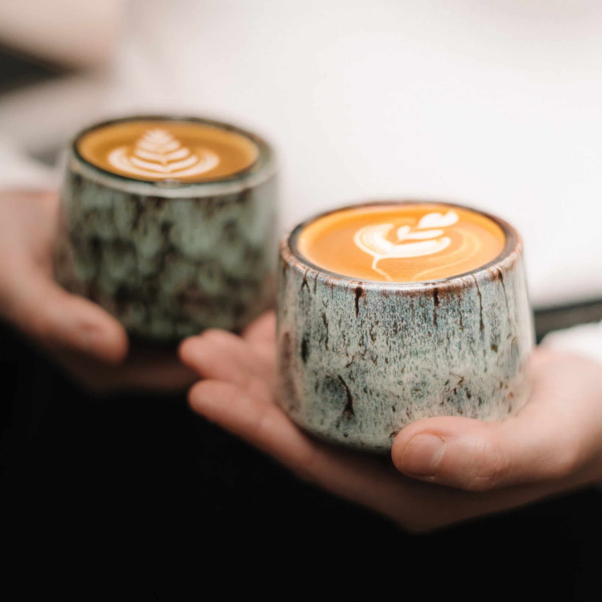 Zwei Cappuccino Tassen präsentiert von einer Frau mit tollem Latte Art darin.