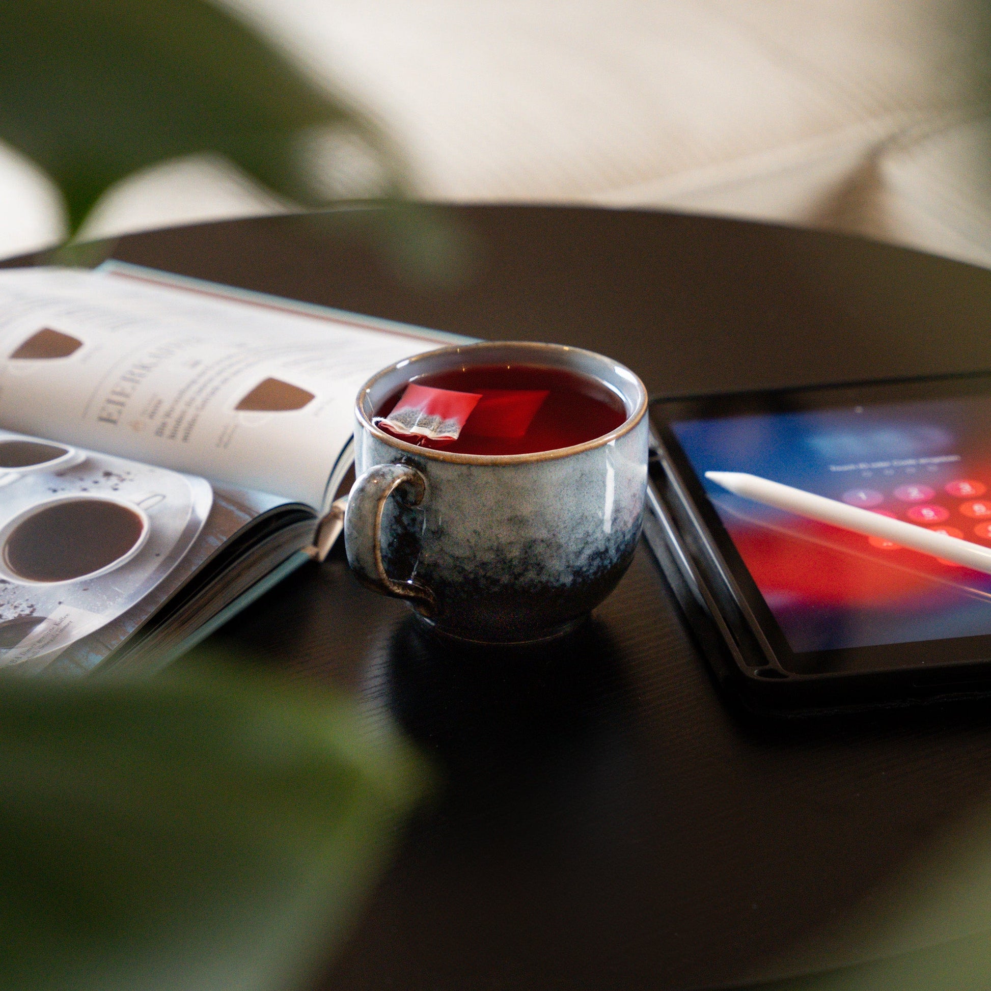 PHENIOX Teetasse Infinity XL steht zwischen einem Tablet und einem Buch auf einem schwarzen Tisch.