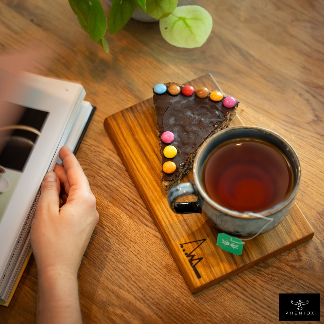 PHENIOX Teetasse Infinity XL gefüllt mit Tee steht auf einem Holzbrettchen zusammen mit einem Stück Kuchen.